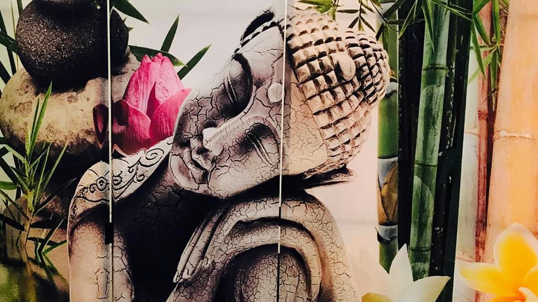 A resting Buddha head beside a pink lotus and bamboo, part of the decor screen in the treatment room