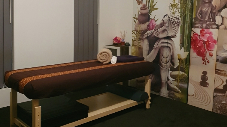 Massage table with brown and saffron Thai-pattern linen, rolled towels and a headrest