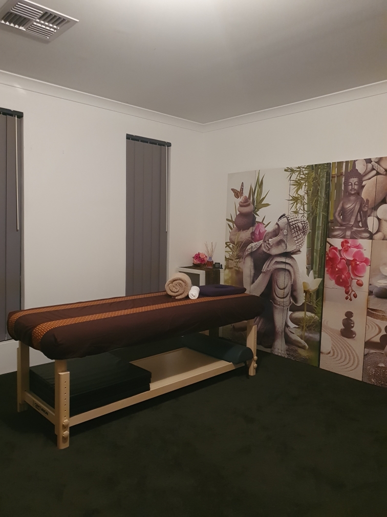 The treatment room at SabaiSabai Aroma Thai Massage, with a massage table dressed in Thai-pattern linen beside a Buddha and orchid screen